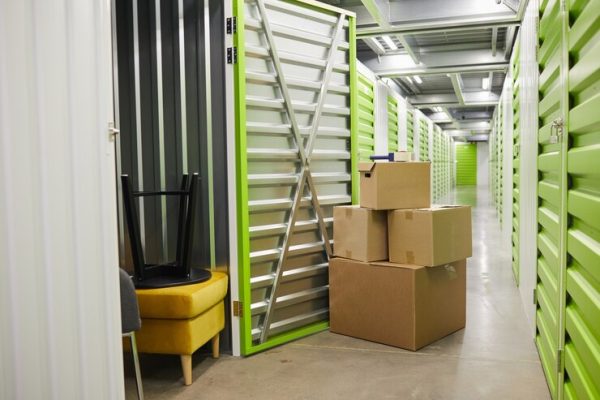 Climate-controlled storage unit with boxes stacked outside and furniture visible inside the unit.