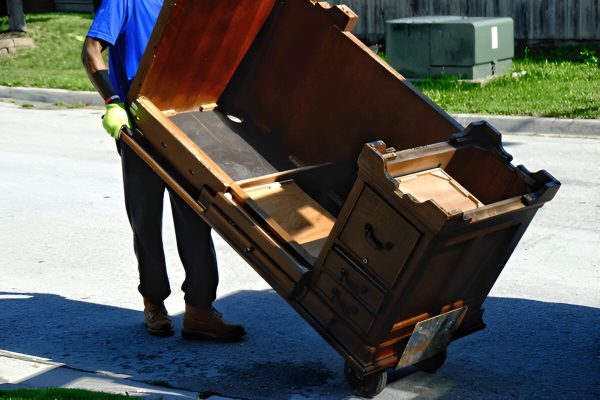 Mover transports heavy wooden furniture safely on a dolly during relocation or junk removal.