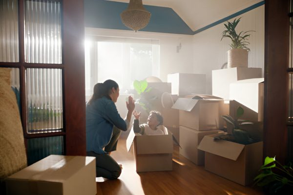 Mom and child play with boxes during move, surrounded by packed items in a bright living room.