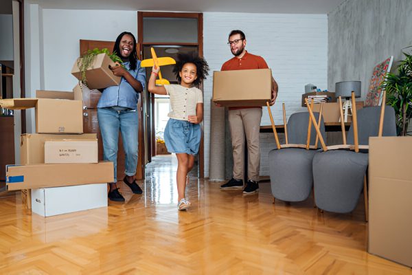 Happy family moving into a new home, carrying boxes while a young girl runs with a toy airplane.