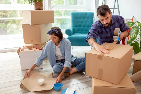 Couple packing household items into boxes, wrapping dishes and sealing cartons for moving day.